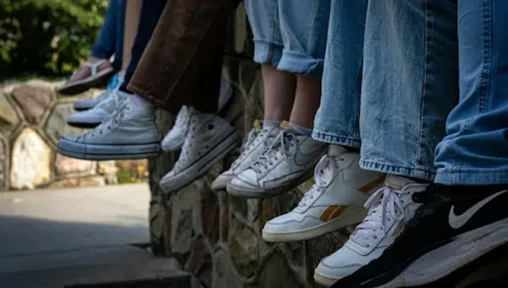 Students sitting on a wall wearing different sneakers, including white Converse, Nike, and Reebok shoes